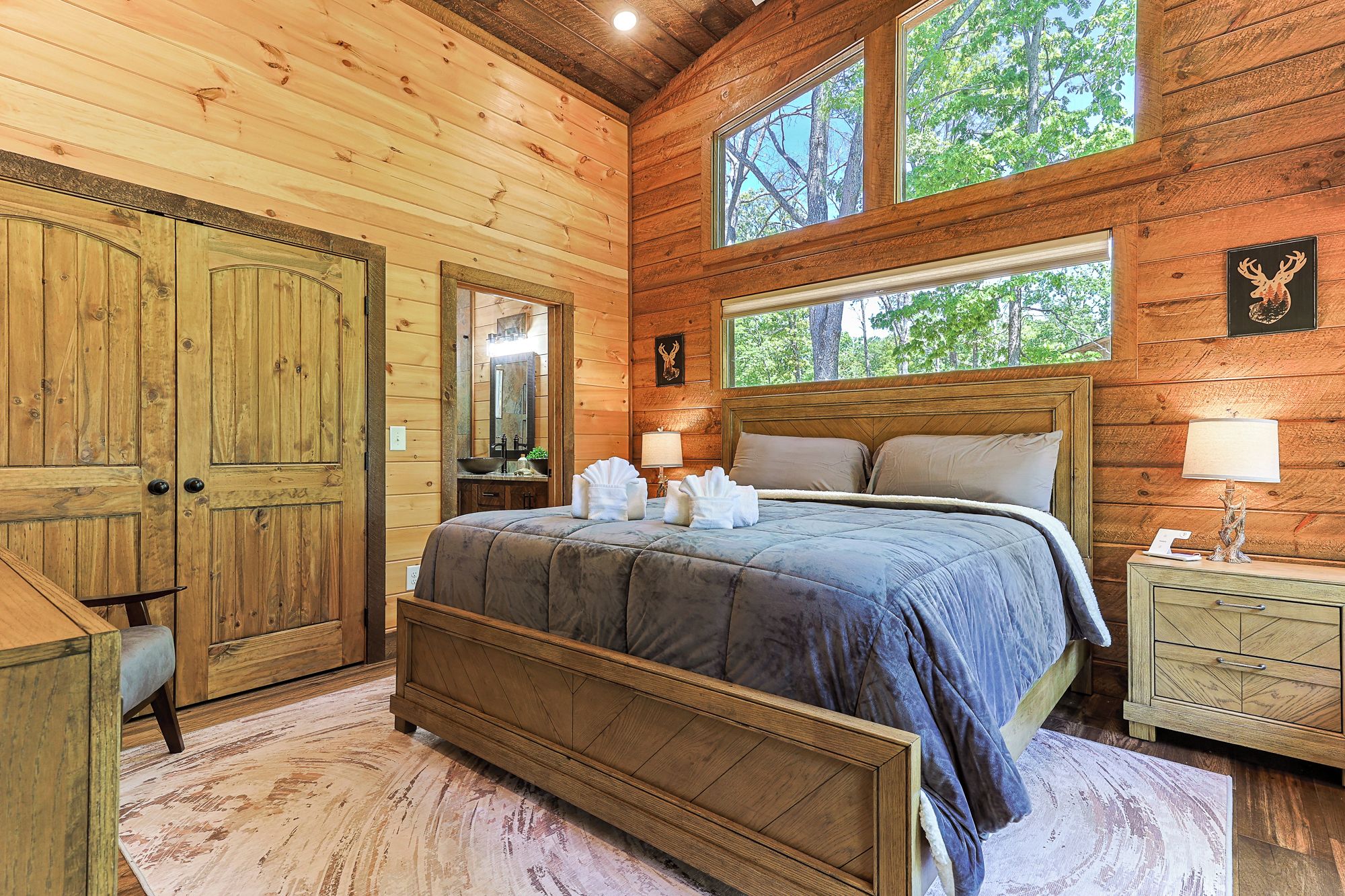 Ein Schlafzimmer einer Holzhütte mit Bett, Schminktisch und großen Fenstern.