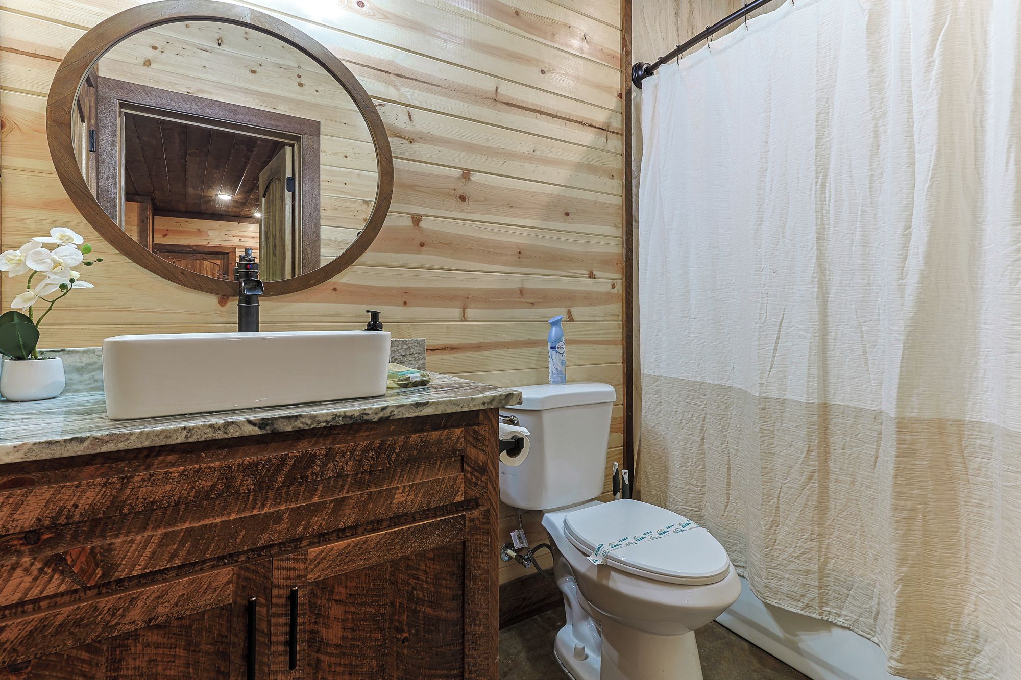 Une salle de bain avec un meuble-lavabo en bois, un évier, un miroir, des toilettes et un rideau de douche.