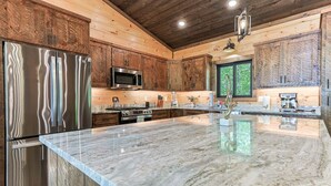 A kitchen with wooden cabinets, stainless steel appliances, a marble countertop, and a large window. - Rugged Trail Oasis: Modern 3BR Cabin w/ 3 Fireplaces & Mountain Views (Morganton)