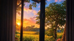 Ein Zimmer mit Blick auf einen Sonnenuntergang über einem Feld, ein Fenster mit Vorhängen und ein Bett.