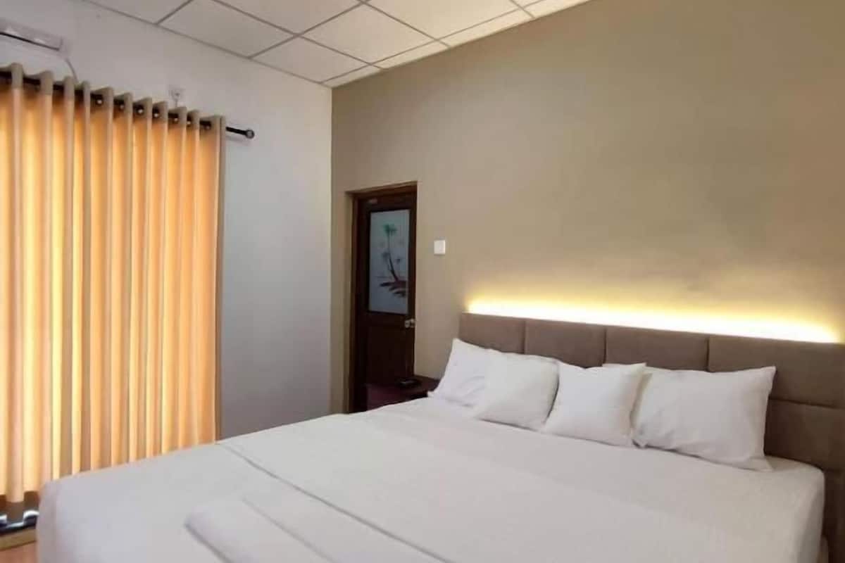 Een hotelkamer met een groot bed, een hoofdeinde met geïntegreerde verlichting, een raam met gordijnen en een deur met een schilderij.