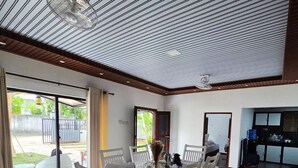 Ein Essbereich mit einem Tisch für vier Personen, umgeben von weißen Stühlen, einem Deckenventilator und Blick ins Freie.