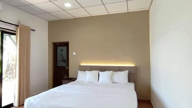 Ein modernes Hotelzimmer mit einem großen Bett, einer Kopfteilbeleuchtung, einem großen Fenster mit Vorhängen und einem Fliesenboden.