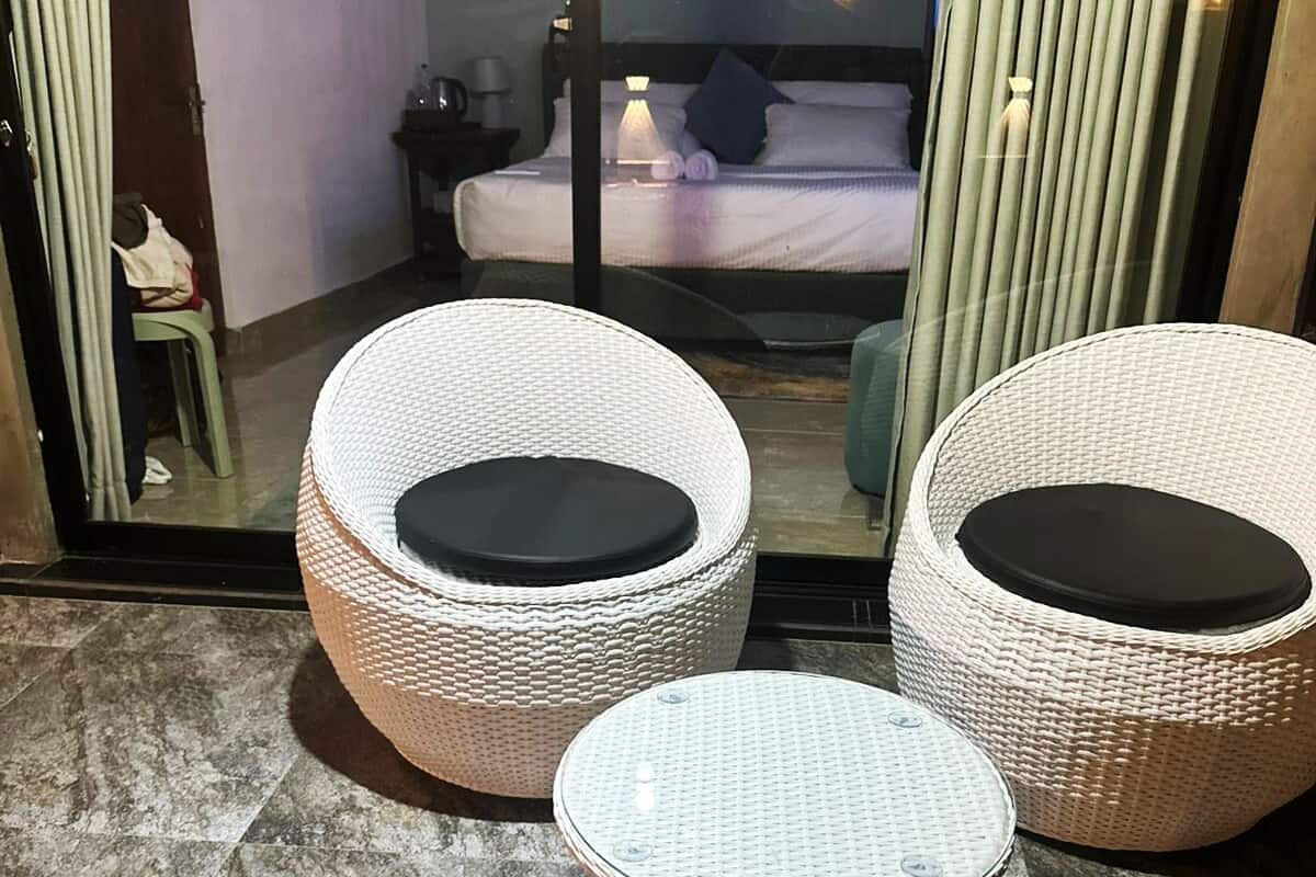 Een kamer met een glazen deur die uitkomt op een balkon met rieten meubels, een bed met matras en kussens.