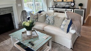 A living room with a fireplace, a sofa, a coffee table, and a TV. - Cheboygan Michigan Escape – River Views & Adventure Nearby.  (Cheboygan)