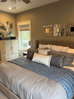 Une chambre à coucher avec un grand lit, une commode, une fenêtre avec des stores et des œuvres d’art décoratives au mur.