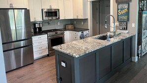 A modern kitchen with white cabinets, stainless steel appliances, a granite countertop, and motivational wall art. - Cheboygan Michigan Escape – River Views & Adventure Nearby.  (Cheboygan)