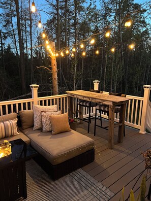 Eine Terrasse mit Sofa, Tisch und Stühlen, umgeben von Bäumen.