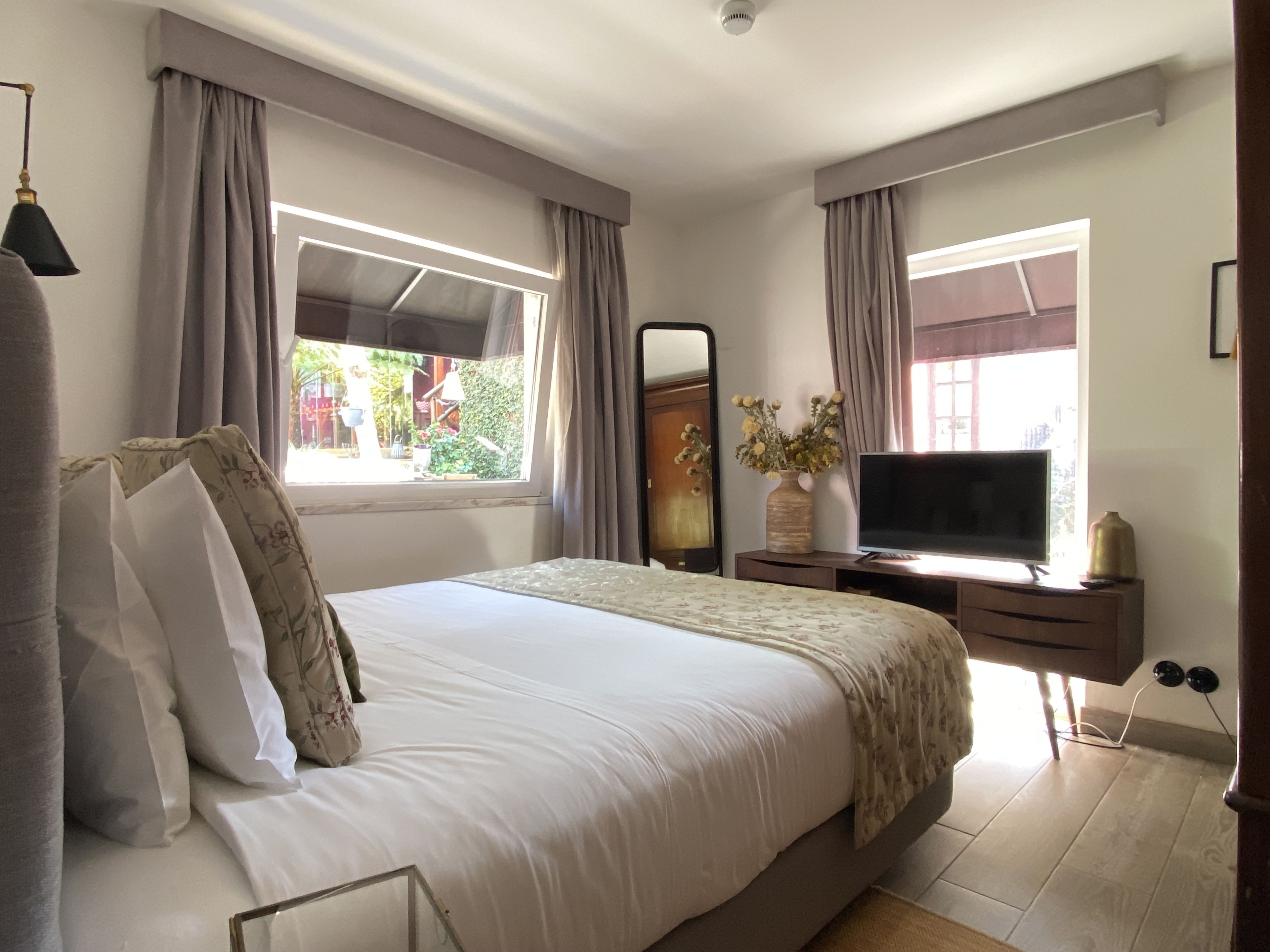 A bedroom with a bed, a television, a dresser, a mirror, and a window with curtains.
