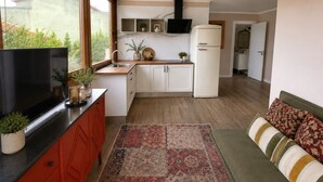 A compact kitchen with a TV, cabinets, a refrigerator, and a window. - Storytellers - Checkinhome- T1 (São Pedro)