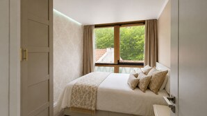 A bedroom with a bed, a window, a wardrobe, and a bedside table. - Storytellers - Checkinhome- T1 (São Pedro)