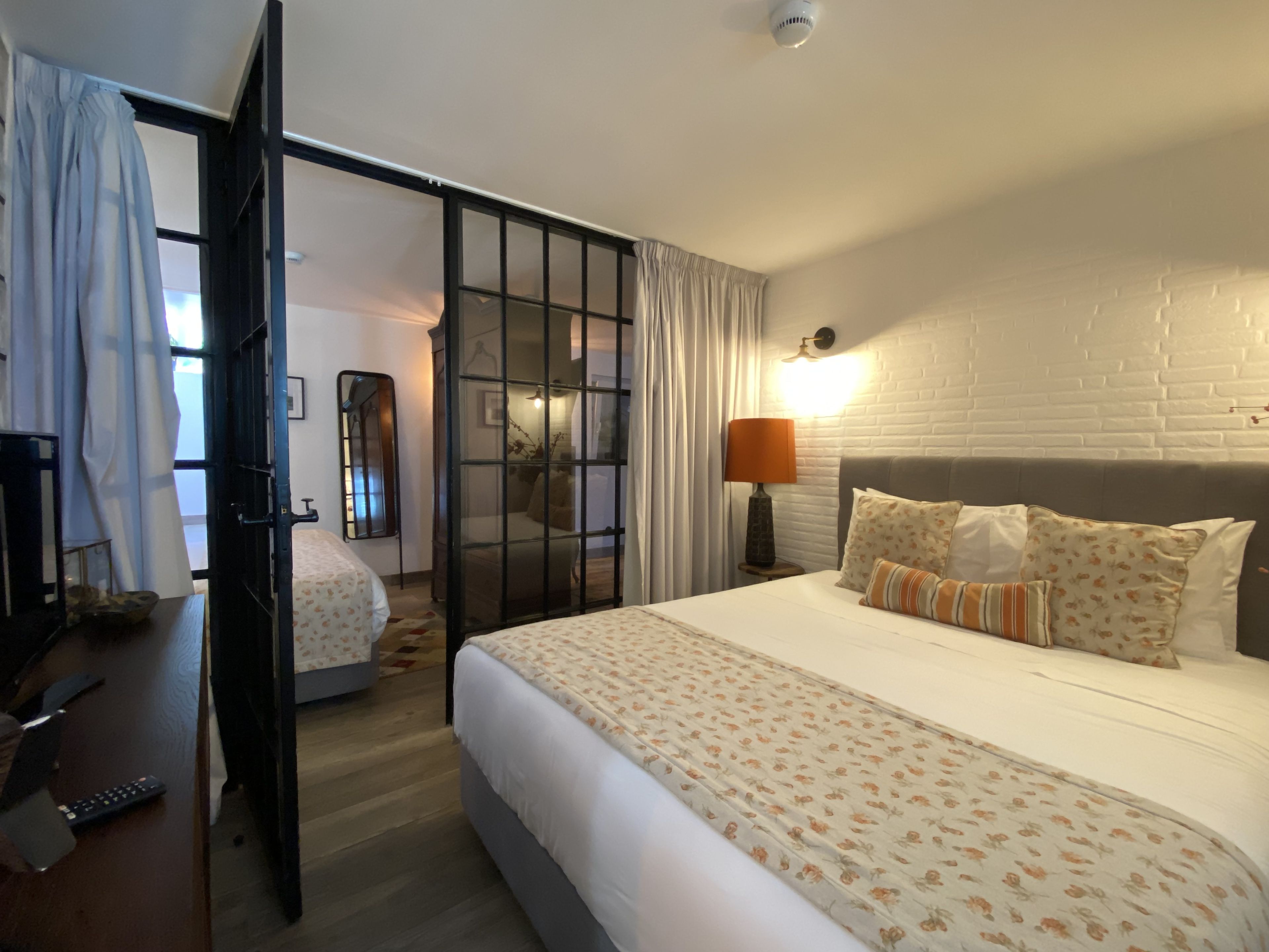 A hotel room with a bed, a desk, a chair, a lamp, and a window with curtains.