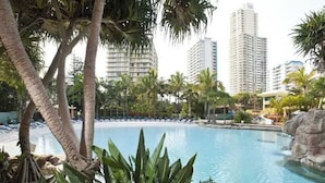 Área de piscina com palmeiras, espreguiçadeiras e vista para prédios altos ao fundo.