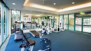 Academia com esteiras, aparelhos de musculação e carpete azul.