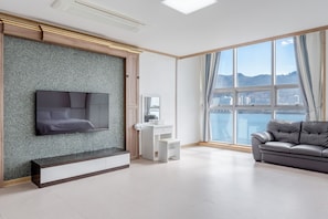 Una sala de estar moderna con un televisor de pantalla plana montado en una pared con textura, una consola blanca, un sofá de cuero gris y un amplio ventanal con vistas a la ciudad.