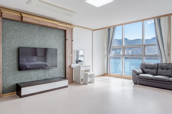 Ein modernes Wohnzimmer mit einem an einer strukturierten Wand montierten Flachbildfernseher, einem weißen Konsolentisch, einem grauen Ledersofa und einem großen Fenster mit Blick auf die Stadt.