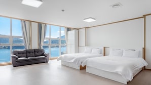 A modern hotel room with a large window offering a scenic view, a sofa, two beds, and a ceiling light. - Yeosu Turtleship Pension (Yeosu)