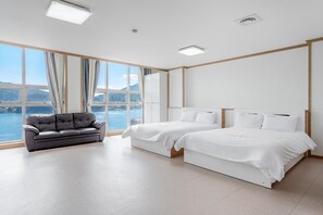 Quarto de hotel moderno com uma janela ampla que oferece uma vista panorâmica, um sofá, duas camas e uma luminária no teto.