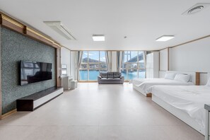 Quarto de hotel moderno com uma janela grande, televisão de tela plana, sofá e duas camas.
