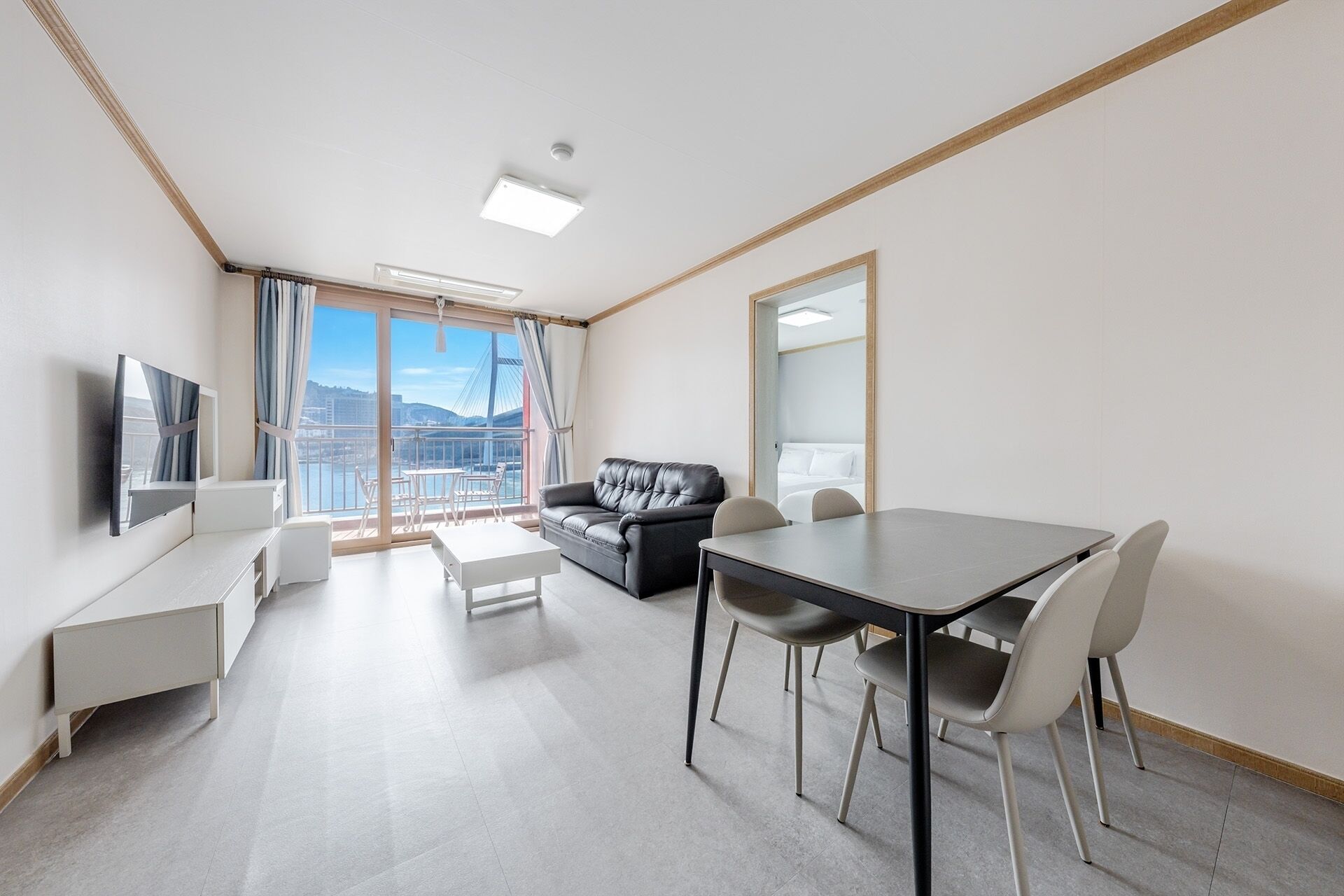 Quarto de hotel moderno com varanda, sofá, mesa de jantar e televisão.