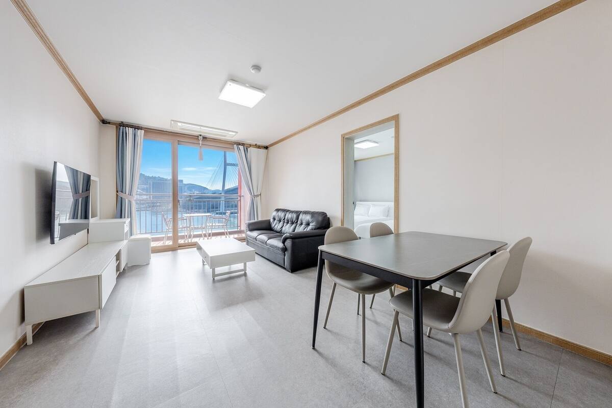 Una habitación de hotel moderna con balcón, sofá, mesa de comedor y televisión.