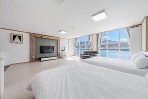 Moderni hotellihuone, jossa on suuri sänky, televisio, oleskelualue ja näkymä vesistöön.