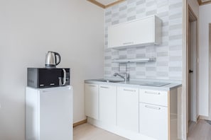 Een kleine keuken met een magnetron, waterkoker, spoelbak en witte kastjes.