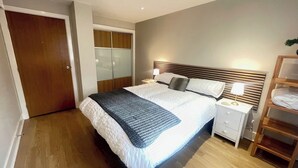 Habitación de hotel con cama, mesitas de noche, un armario y una mesita con lámpara.