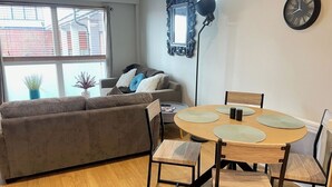 Una sala de estar moderna con un sofá, una mesa de comedor con sillas, un reloj de pared y una ventana con persianas.