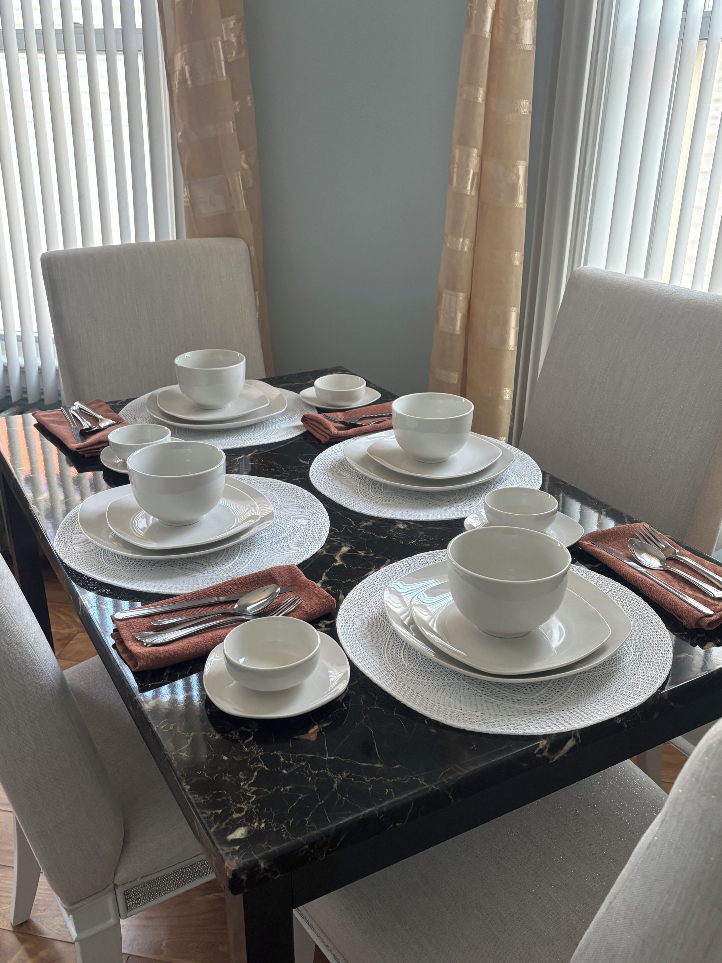 A dining table set with white bowls and plates, silverware, and brown napkins.