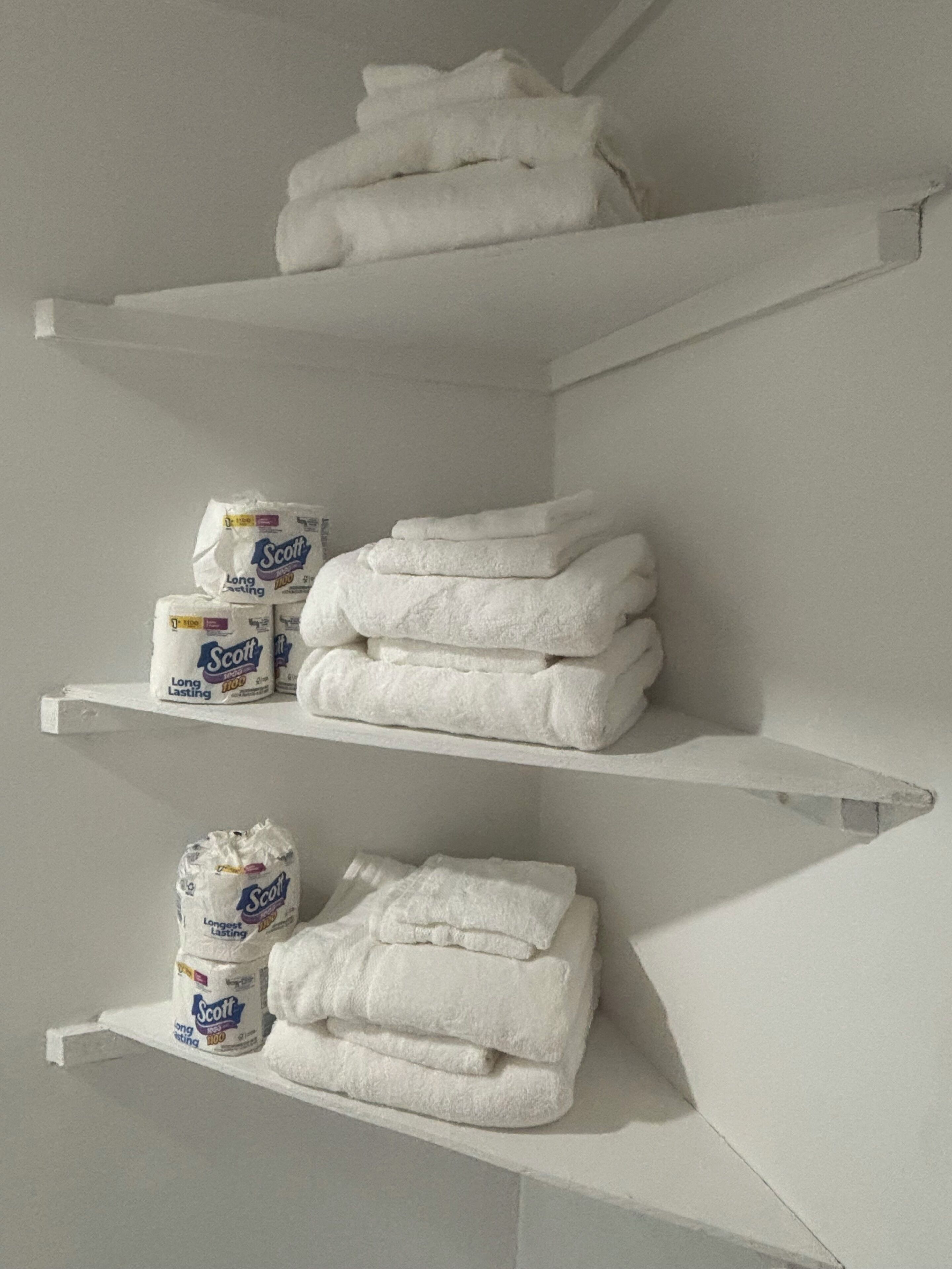 A bathroom with white shelves holding towels and toilet paper.