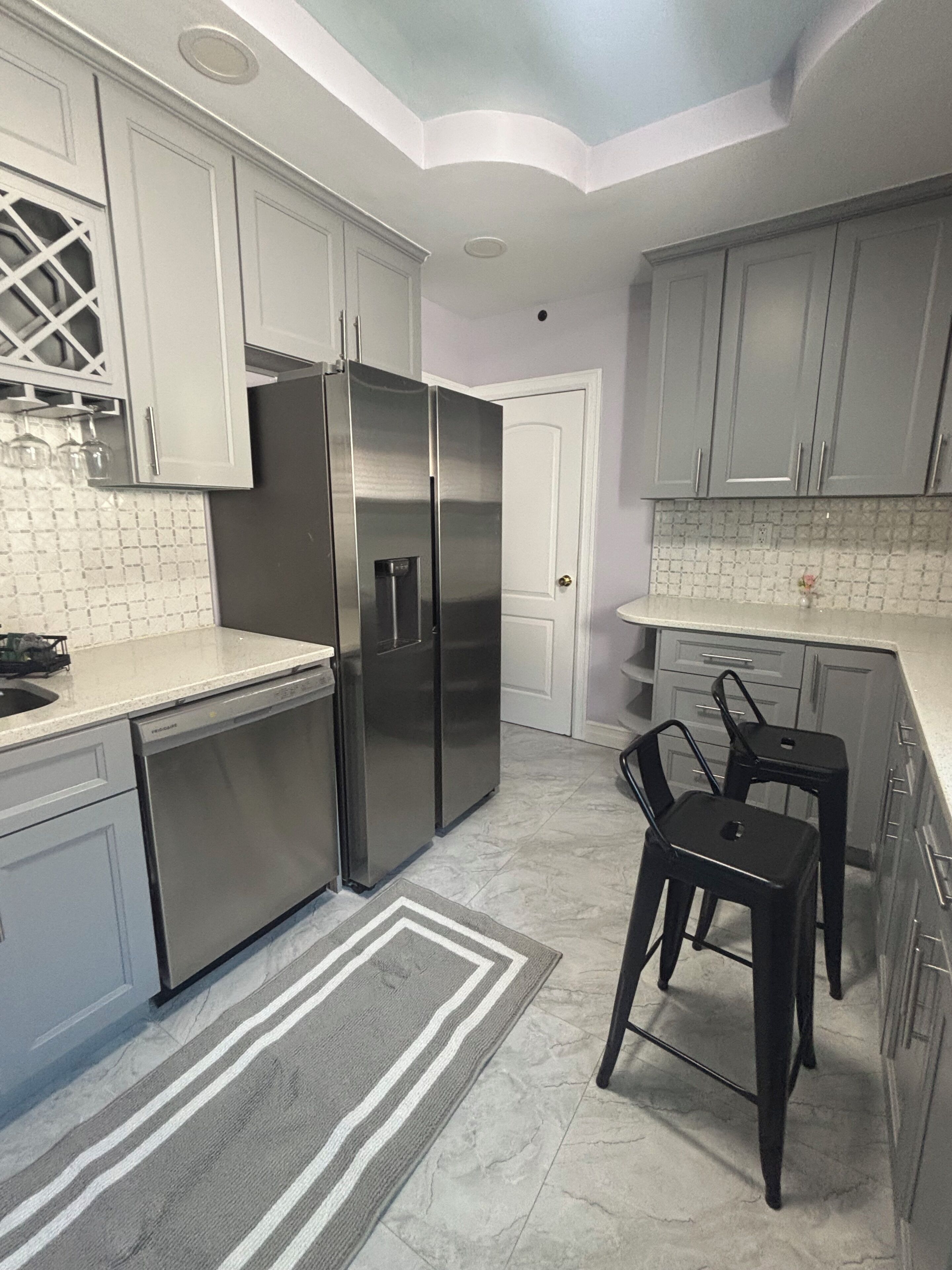 A compact kitchen with stainless steel appliances, a tiled backsplash, and a small dining area with stools.