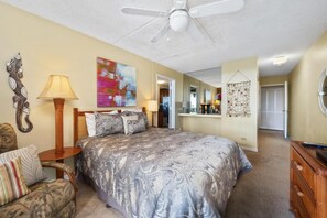 A bedroom with a bed, a chair, a lamp, a ceiling fan, and a painting on the wall. - Kona Pacific A202 - Oceanview Kona Condo | Walk to Town & Ironman (Kailua Kona)
