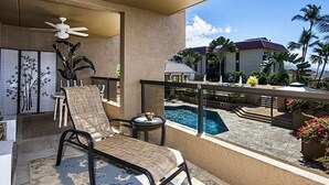 Varanda com cadeira, mesa pequena, ventilador de teto e vista para uma piscina e palmeiras.