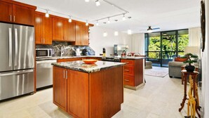 A modern kitchen with wooden cabinets, stainless steel appliances, and a large island. - Kona Pacific B411 - Garden View Kona Condo | Walk to Town & Ironman (Kailua Kona)