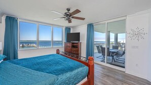 Quarto com cama, ventoinha no teto, televisão e varanda com mesa e cadeiras.