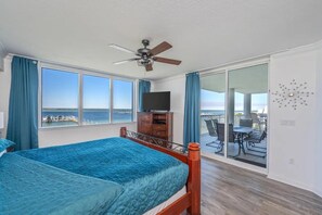 A bedroom with a bed, a ceiling fan, a TV, and a balcony with a table and chairs. - Beachin' Escape | Destin West Lazy River | Huge Balcony | Bay Views | Sleeps 10 (Fort Walton Beach)