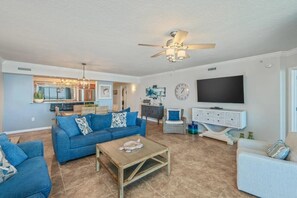 A living room with a blue sofa, a coffee table, a TV, and a ceiling fan. - Beachin' Escape | Destin West Lazy River | Huge Balcony | Bay Views | Sleeps 10 (Fort Walton Beach)