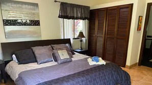Une chambre à coucher comprenant un lit, une table de chevet, une lampe, une fenêtre avec des rideaux et une armoire.