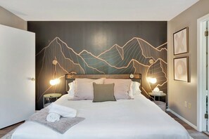 Habitación de hotel con una cama, cabecera con diseño de montaña, lámparas de noche, mesita de noche y un reloj de pared.