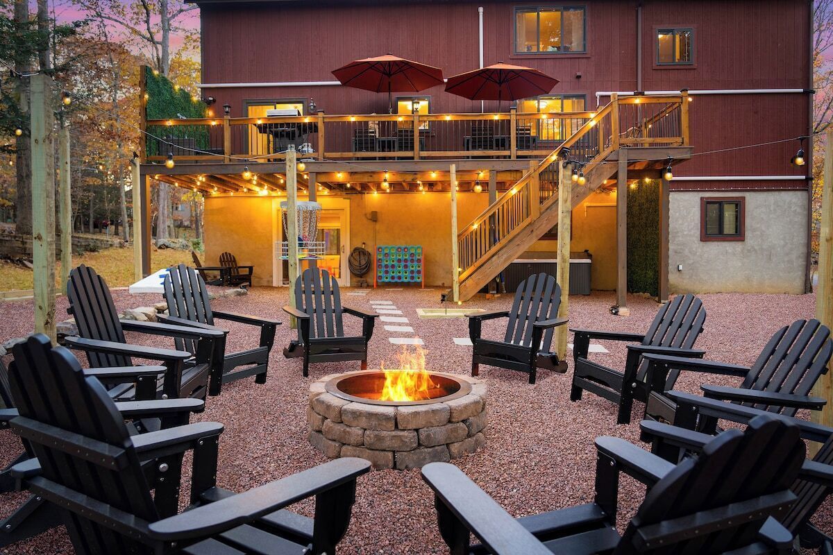 Un foyer entouré de fauteuils Adirondack, une terrasse couverte avec des parasols et un escalier menant à un niveau supérieur.
