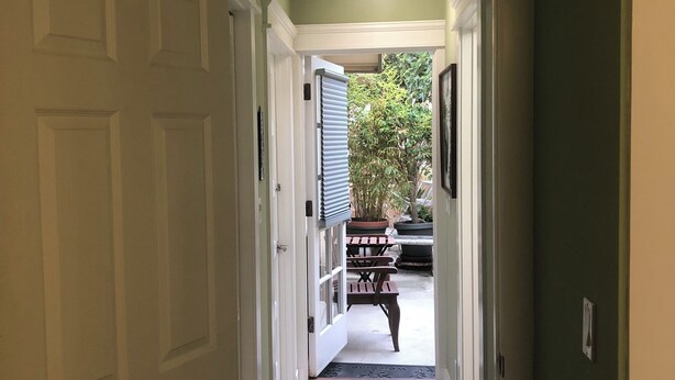 Un pasillo con una puerta, una planta en maceta y vistas a un espacio exterior con una mesa y sillas.