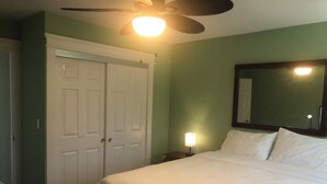 Un dormitorio con cama, ventilador de techo, mesita de noche con lámpara y armario.