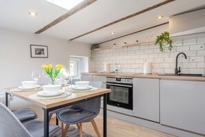 A modern kitchen with white cabinetry, a wooden countertop, and a dining area with a table set for two. - Powstańców Skyline Loft Apartment (Katowice)