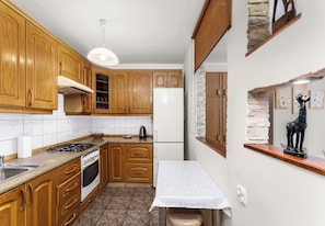 A kitchen with wooden cabinets, a stove, a refrigerator, and a table with a newspaper. - Grzegórzki Homely Apartment (Kraków)