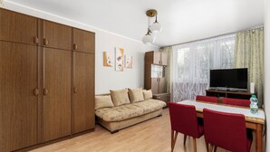 Una habitación con sofá, una mesa de comedor con sillas, televisión y armario.