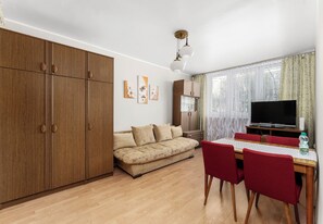 Ein Zimmer mit einer Couch, einem Esstisch mit Stühlen, einem Fernseher und einem Kleiderschrank.