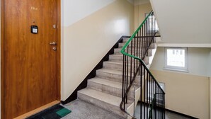 Una puerta de madera con una placa numérica, una escalera con barandillas verdes y un ventanal pequeño en la parte superior.