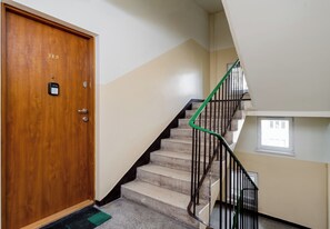 Eine Holztür mit Schild, eine Treppe mit grünen Geländern und ein kleines Fenster auf der oberen Landung.