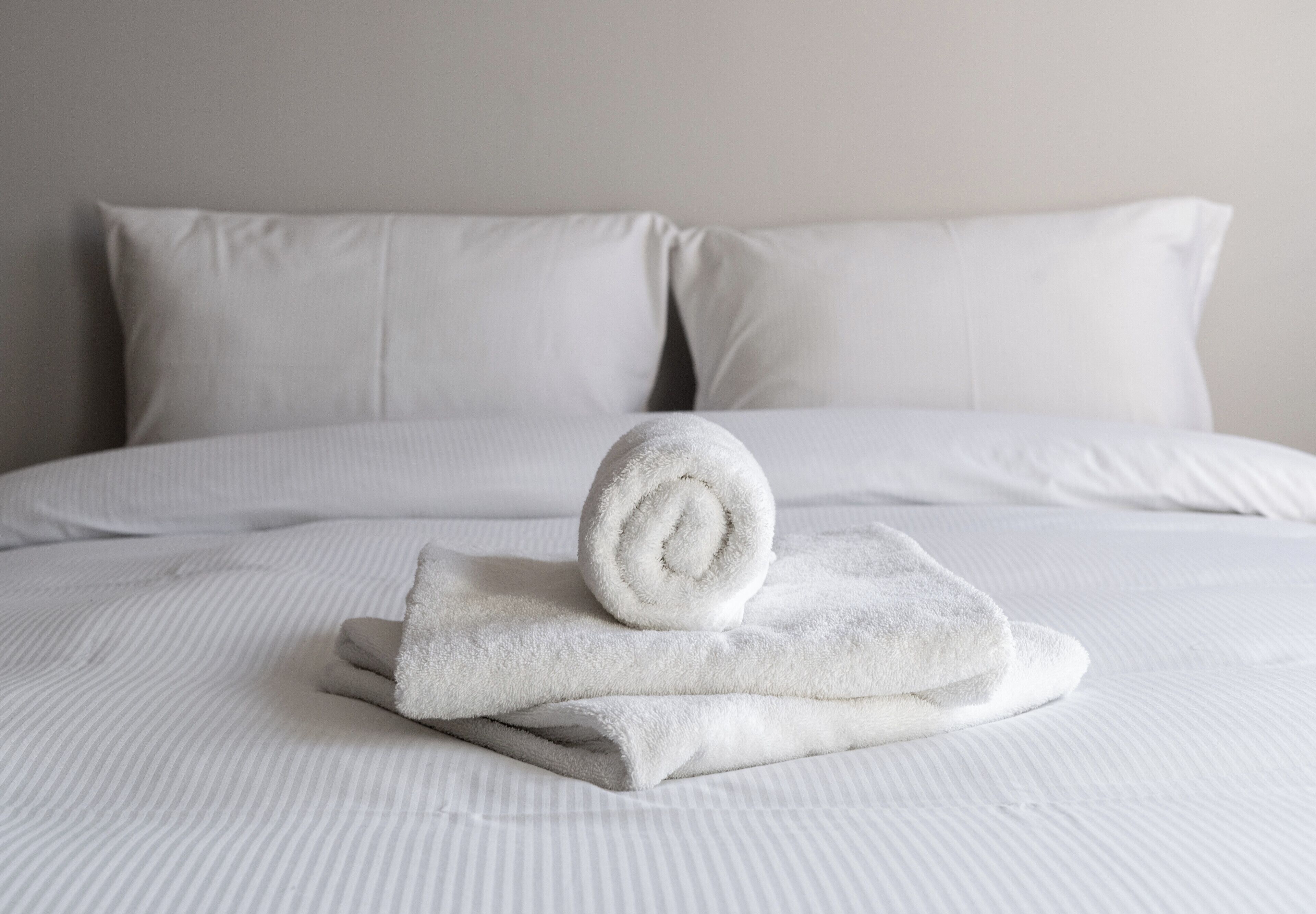 Una cama bien tendida con sábanas y almohadas blancas, una toalla enrollada y una colcha a rayas.